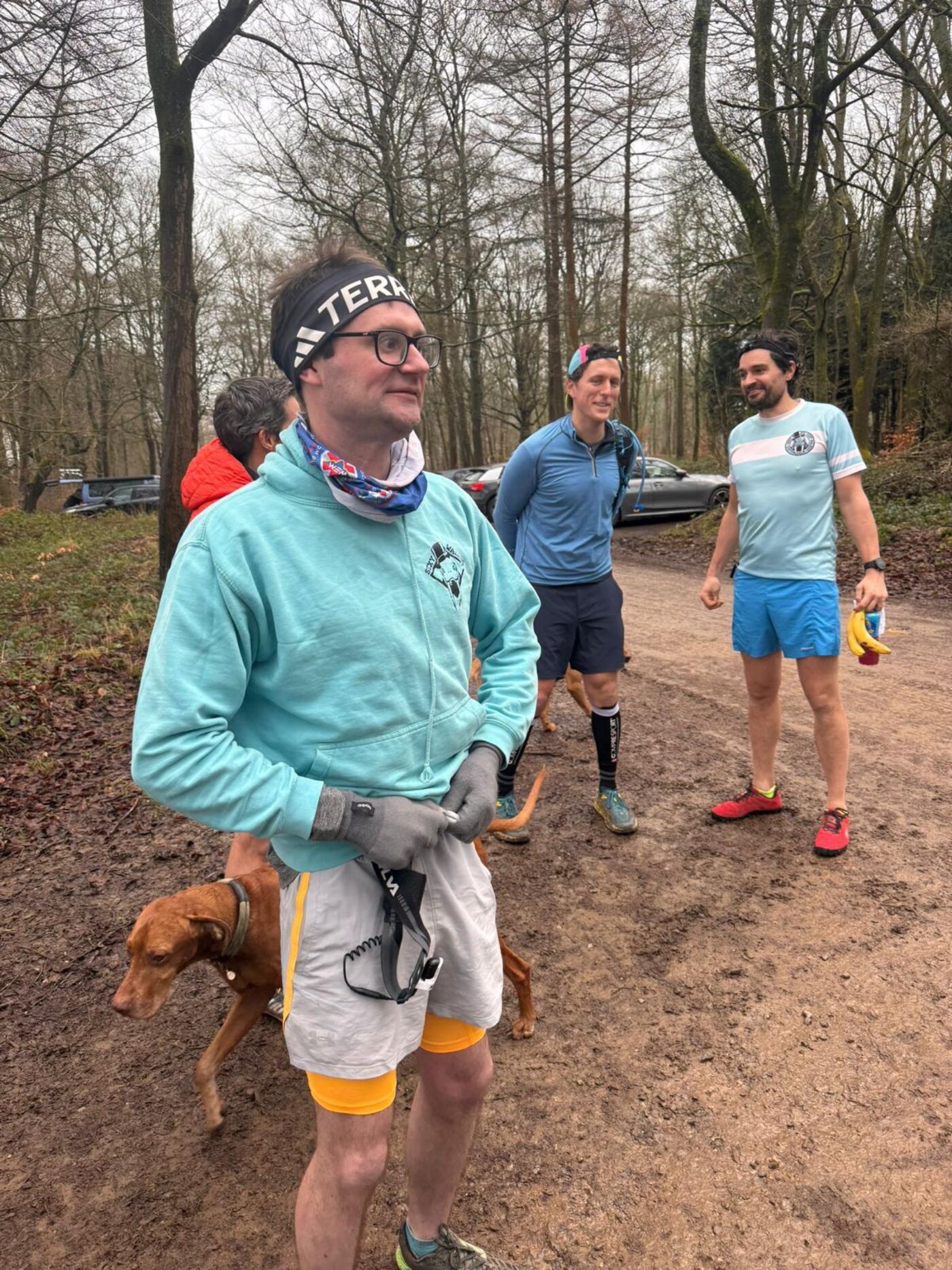 Club members in a muddy forest car park with two dogs and a member in the club hooded top