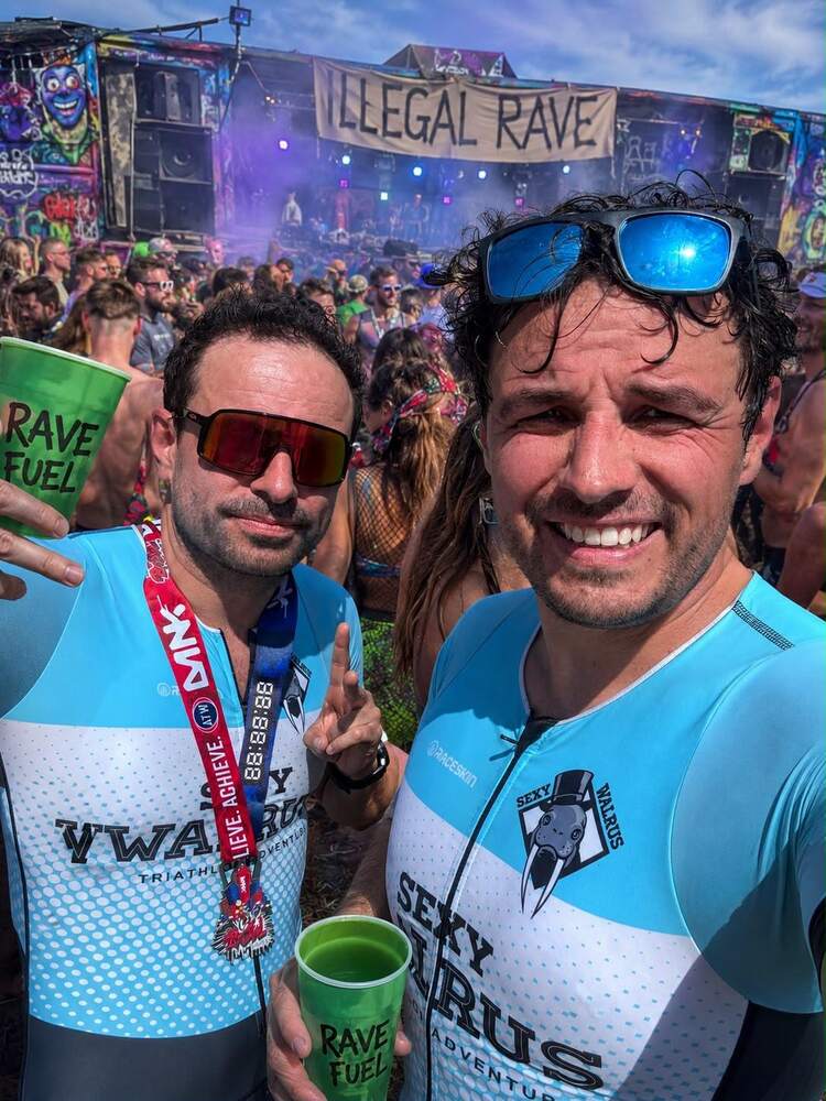 Two members with medals and a drink in front of an event banner