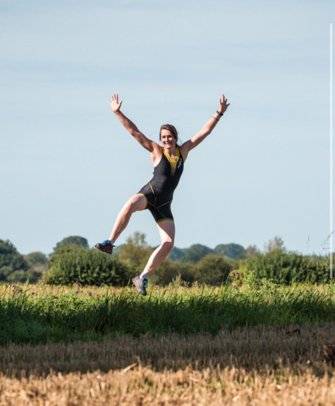 A club member in a tri-suit jumping in the air with both arms up after finishing