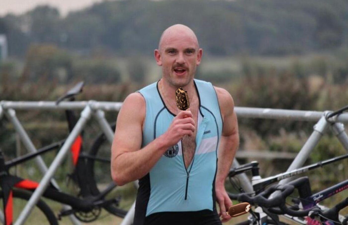 A member in the club tri-suit in a transition area, holding a medal, bicycles behind him