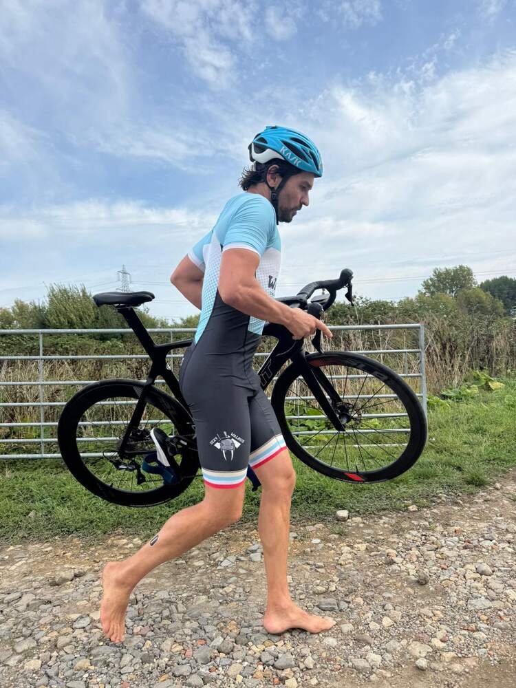 A member in a tri-suit walking with the bicycle, helmet on, shoes off